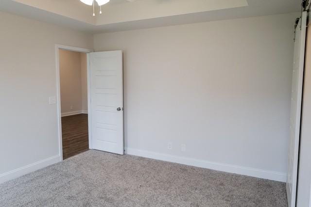 carpeted empty room featuring a ceiling fan, a tray ceiling, baseboards, and a barn door