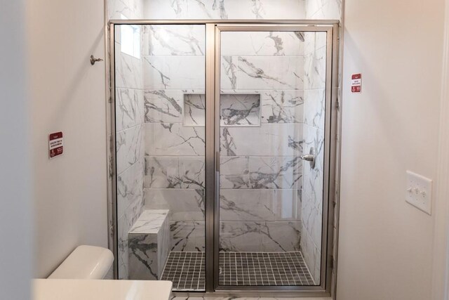 bathroom with toilet and a marble finish shower