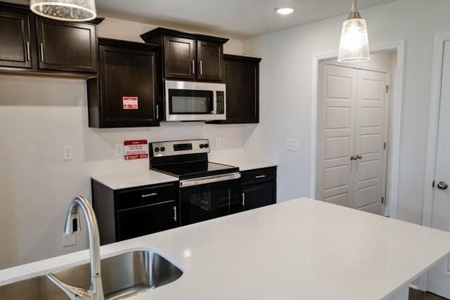 kitchen with light countertops, appliances with stainless steel finishes, a sink, and decorative light fixtures