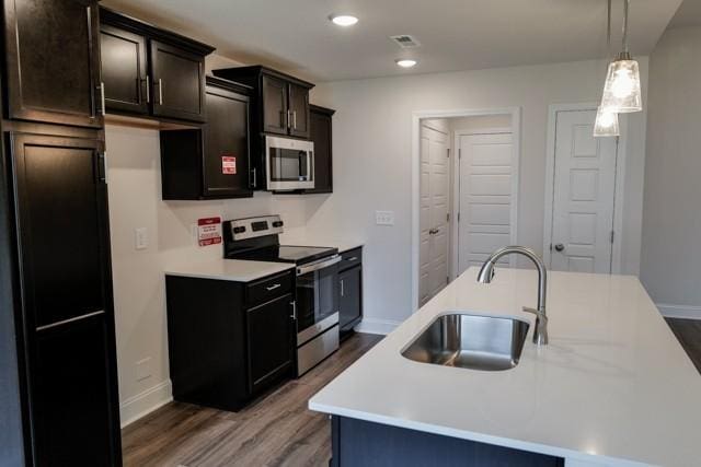 kitchen featuring stainless steel appliances, wood finished floors, a sink, and light countertops