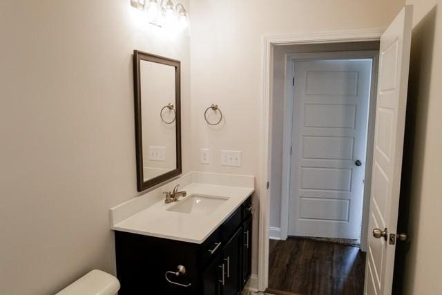 half bathroom with toilet, wood finished floors, and vanity