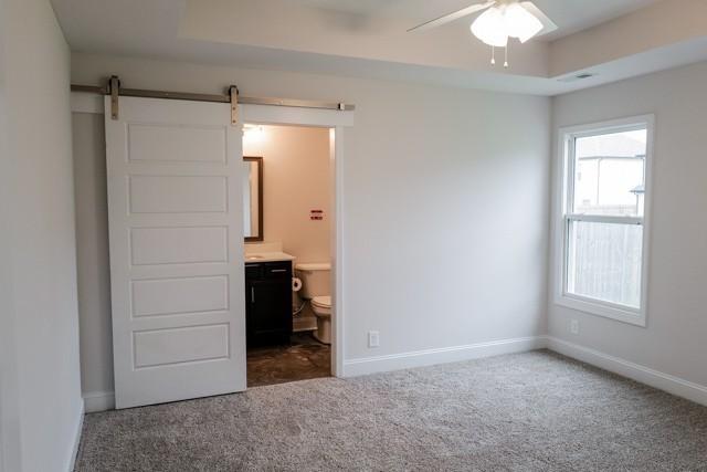 unfurnished bedroom featuring a barn door, connected bathroom, carpet floors, baseboards, and a raised ceiling