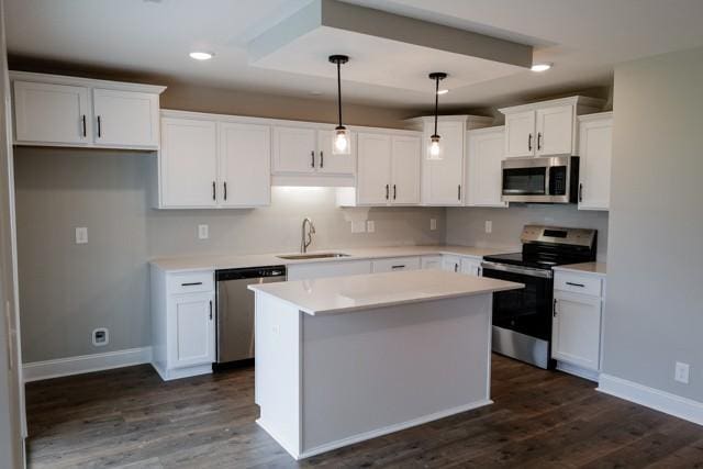 kitchen with appliances with stainless steel finishes, a center island, white cabinetry, sink, and hanging light fixtures