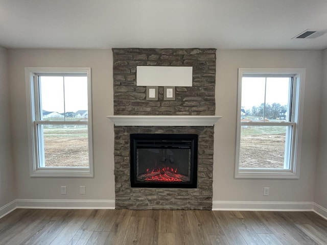 unfurnished living room featuring a wealth of natural light, a fireplace, wood finished floors, and visible vents