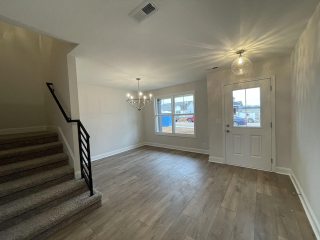 entrance foyer featuring wood finished floors, visible vents, baseboards, stairway, and an inviting chandelier