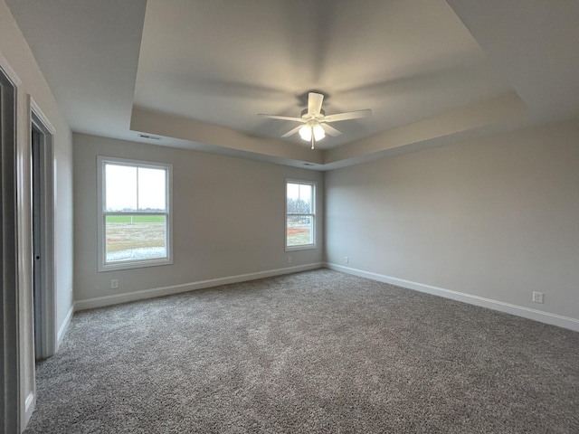 carpeted spare room featuring a raised ceiling, ceiling fan, and baseboards