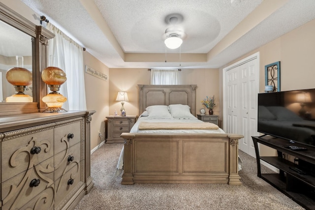 bedroom with ceiling fan, a tray ceiling, a closet, light colored carpet, and a textured ceiling