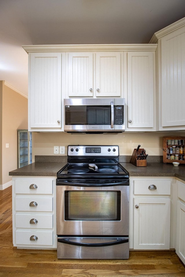 kitchen featuring white cabinets, ornamental molding, light wood-type flooring, and appliances with stainless steel finishes