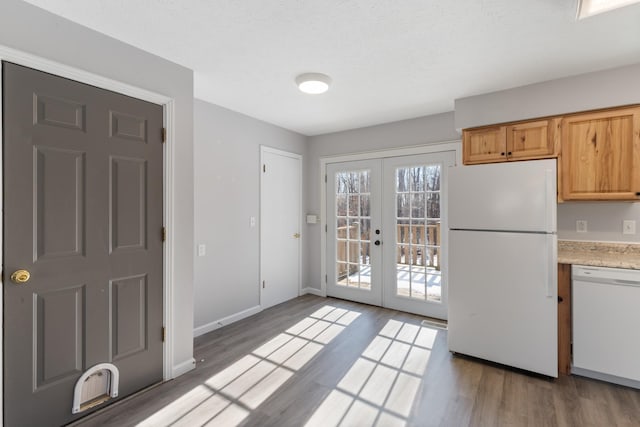 kitchen with a textured ceiling, french doors, white appliances, light brown cabinets, and wood-type flooring