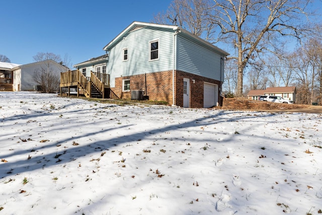 snow covered house with central AC unit, a garage, and a wooden deck