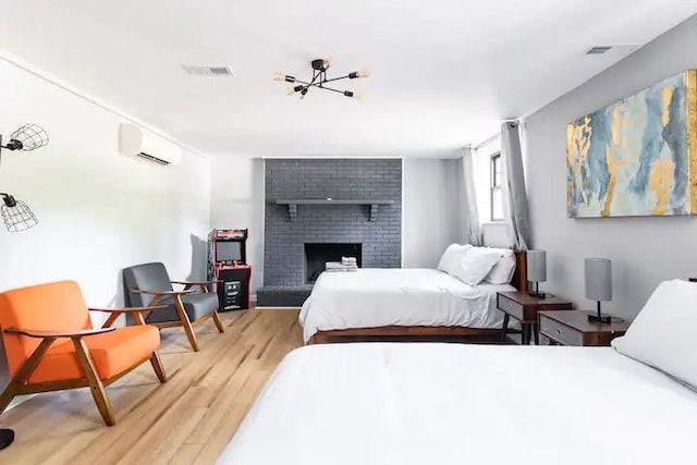 bedroom with a brick fireplace, an inviting chandelier, a wall unit AC, and light hardwood / wood-style floors