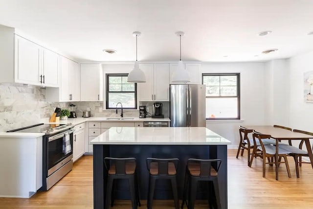 kitchen featuring stainless steel appliances, a center island, sink, white cabinetry, and decorative light fixtures