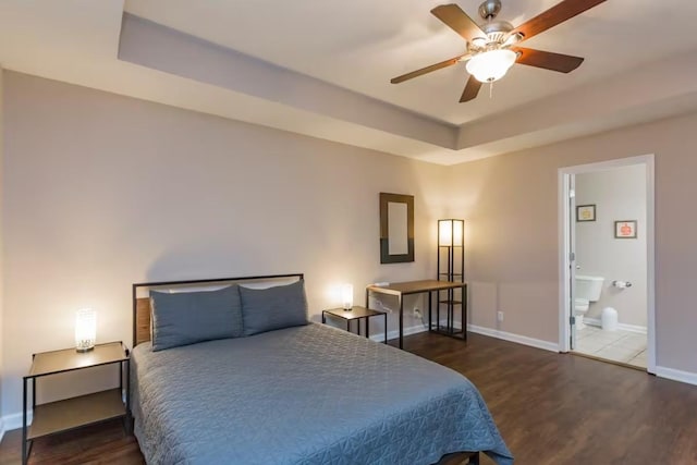 bedroom with ceiling fan, a tray ceiling, dark hardwood / wood-style floors, and connected bathroom