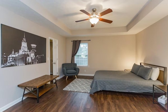 bedroom with a raised ceiling, ceiling fan, and dark wood-type flooring