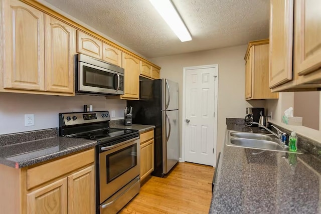 kitchen featuring stainless steel appliances, a textured ceiling, light brown cabinetry, and sink