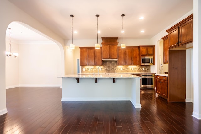 kitchen with appliances with stainless steel finishes, hanging light fixtures, an island with sink, and a breakfast bar