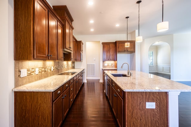 kitchen with sink, a center island with sink, black electric stovetop, and hanging light fixtures