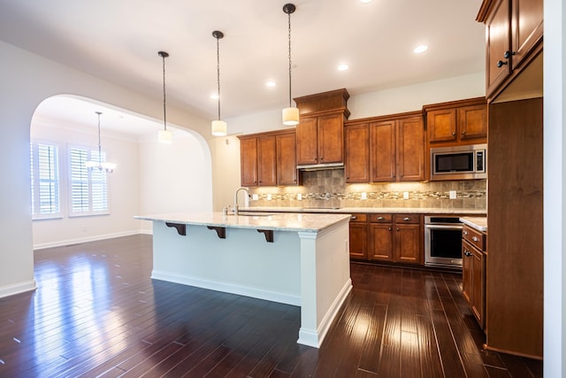 kitchen with appliances with stainless steel finishes, a kitchen breakfast bar, decorative light fixtures, and a kitchen island with sink