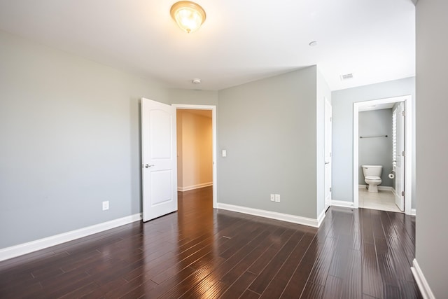 unfurnished bedroom with ensuite bathroom and dark hardwood / wood-style floors