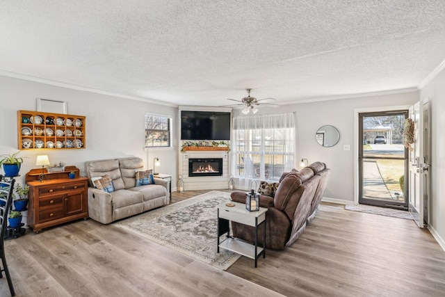 living room featuring a textured ceiling, hardwood / wood-style floors, ornamental molding, ceiling fan, and a large fireplace