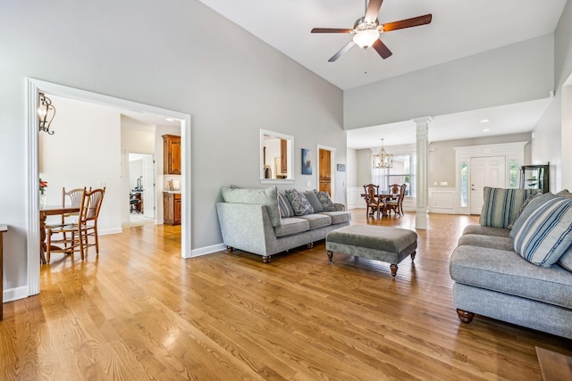 living room with a towering ceiling, ceiling fan with notable chandelier, decorative columns, and light hardwood / wood-style flooring