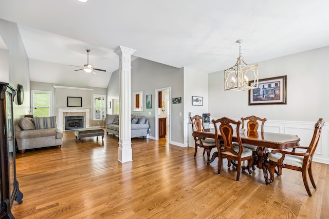 dining space with ceiling fan with notable chandelier, lofted ceiling, a fireplace, and light wood-type flooring