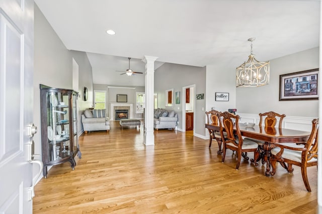 dining space featuring ornate columns, ceiling fan with notable chandelier, lofted ceiling, and light hardwood / wood-style floors