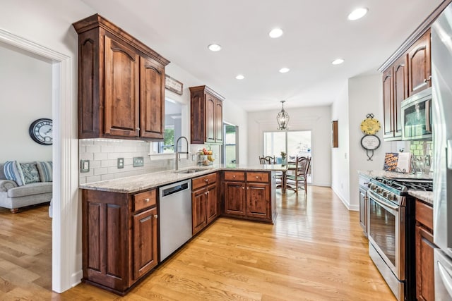 kitchen featuring stainless steel appliances, sink, light hardwood / wood-style flooring, kitchen peninsula, and pendant lighting