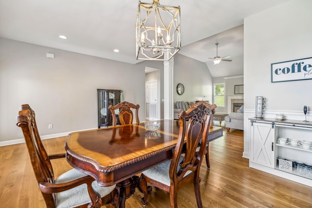 dining space with ceiling fan with notable chandelier, a fireplace, light hardwood / wood-style floors, and lofted ceiling