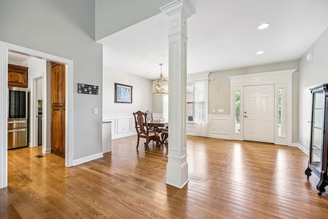 foyer entrance with light hardwood / wood-style flooring, a chandelier, and ornate columns