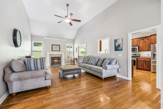 living room with high vaulted ceiling, a tiled fireplace, ceiling fan, and wood-type flooring