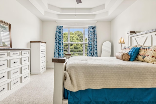 bedroom featuring a raised ceiling, light carpet, and ceiling fan