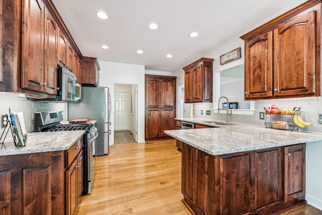 kitchen with stainless steel appliances, kitchen peninsula, light stone counters, sink, and light hardwood / wood-style flooring