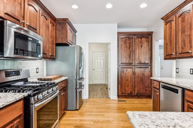 kitchen with light hardwood / wood-style floors, stainless steel appliances, light stone counters, and tasteful backsplash