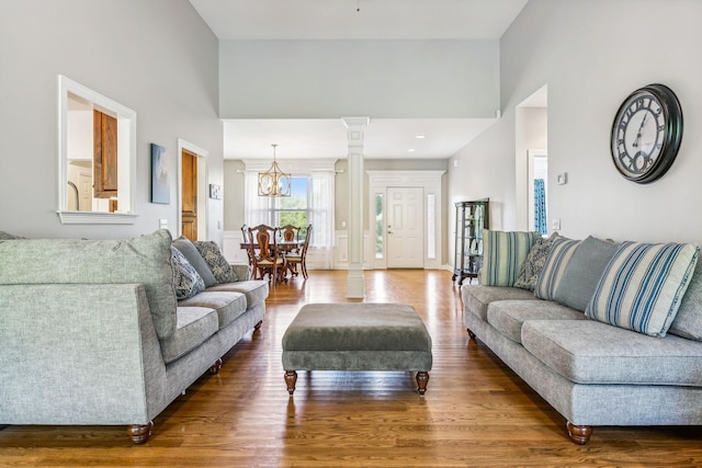 living room featuring a towering ceiling, wood-type flooring, a chandelier, and decorative columns