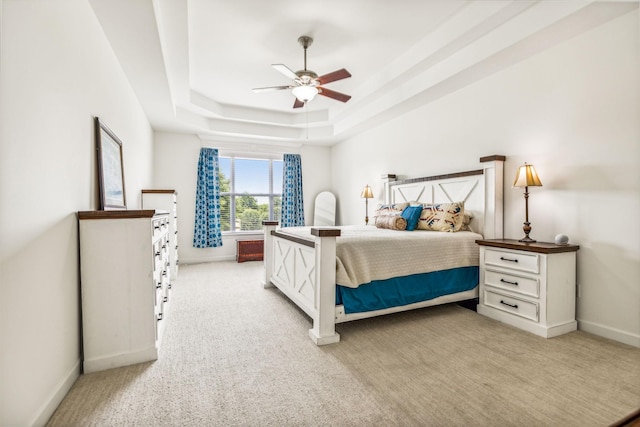 bedroom with a raised ceiling, ceiling fan, and light carpet