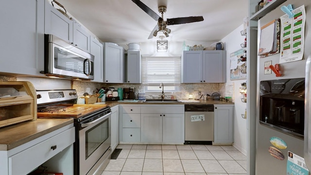 kitchen featuring light tile patterned floors, backsplash, appliances with stainless steel finishes, ceiling fan, and sink