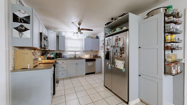 kitchen featuring stainless steel appliances, light tile patterned floors, ceiling fan, sink, and tasteful backsplash