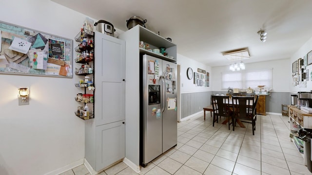 kitchen with wood walls, stainless steel fridge with ice dispenser, light tile patterned floors, and a chandelier