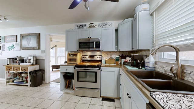 kitchen with stainless steel appliances, tasteful backsplash, light tile patterned flooring, ceiling fan, and sink