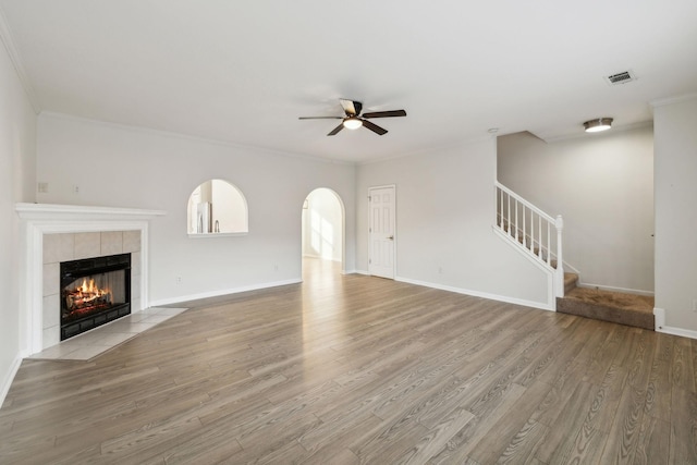 unfurnished living room with a tile fireplace, crown molding, ceiling fan, and light wood-type flooring