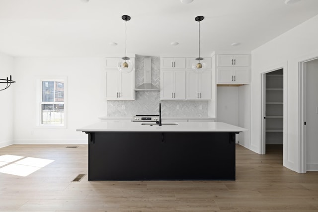 kitchen with white cabinetry, a center island with sink, wall chimney exhaust hood, and sink