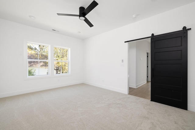 empty room with carpet floors, ceiling fan, and a barn door