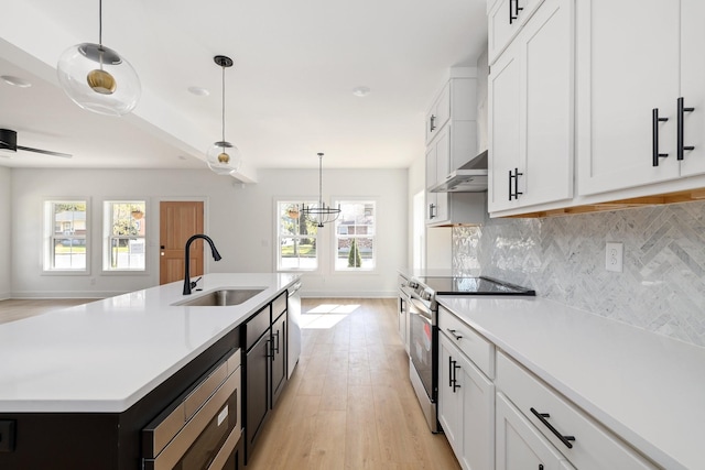 kitchen featuring a kitchen island with sink, appliances with stainless steel finishes, white cabinets, decorative light fixtures, and sink