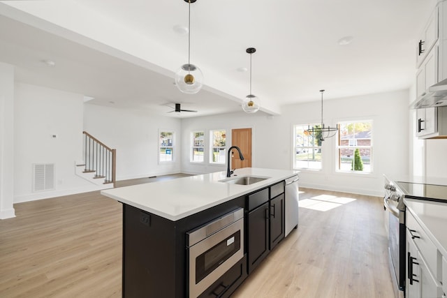 kitchen featuring sink, stainless steel appliances, white cabinets, an island with sink, and ceiling fan with notable chandelier