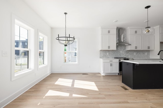 kitchen featuring electric stove, wall chimney exhaust hood, pendant lighting, and white cabinetry