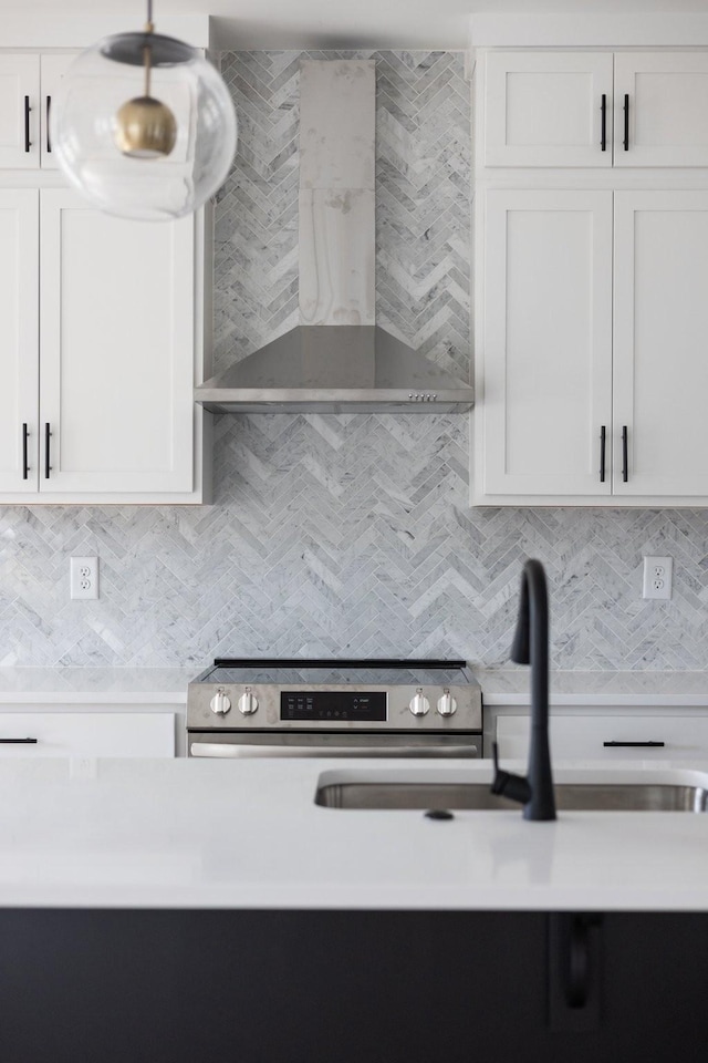 kitchen featuring electric range, wall chimney exhaust hood, tasteful backsplash, and white cabinetry