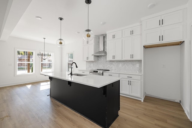 kitchen with white cabinets, a center island with sink, wall chimney range hood, and sink