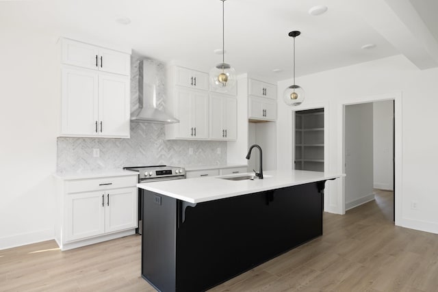 kitchen with sink, white cabinets, wall chimney range hood, and an island with sink