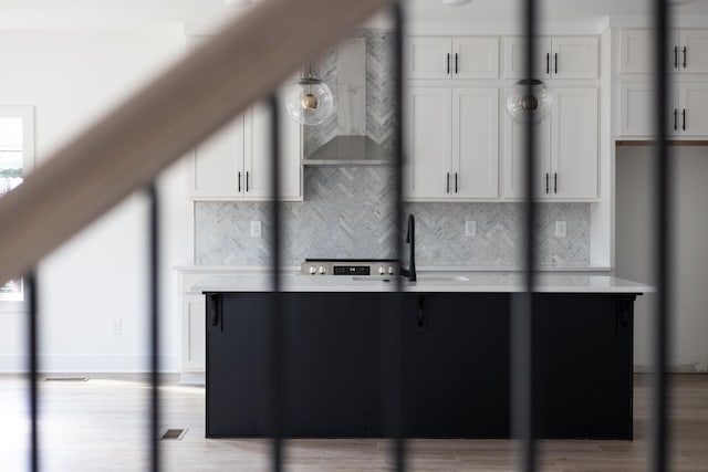 kitchen with wall chimney exhaust hood, backsplash, and white cabinetry